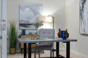 A cozy home office setup featuring a sleek computer table with a laptop, an ergonomic office chair, a tall floor lamp providing soft lighting, a lush green potted plant adding a touch of nature, a vibrant wall painting for decor, and a compact wooden storage unit to neatly organize office essentials.